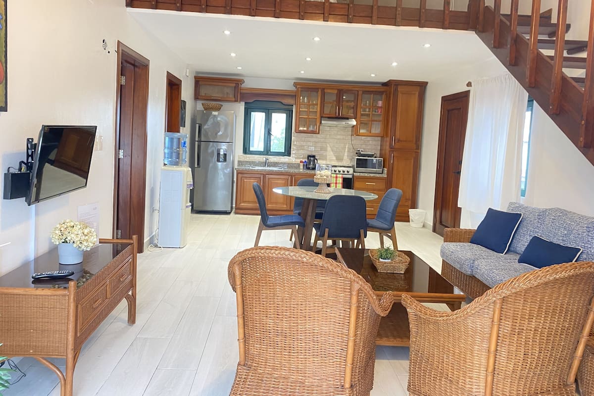 A modern kitchen with wooden cabinets, a stainless steel refrigerator, and a dining area with wicker furniture.