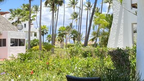 Un jardín tropical con palmeras y una edificación de techo de paja.