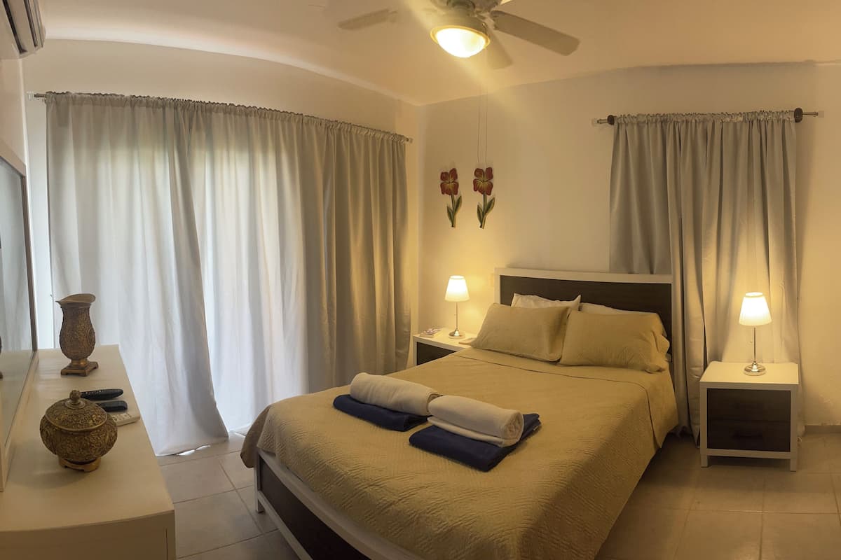 A hotel room with a bed, two bedside tables, a lamp on each table, a TV, and a decorative vase.