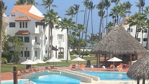 Un resort con un amplio área de piscina, sillas de descanso y sombrillas de paja.