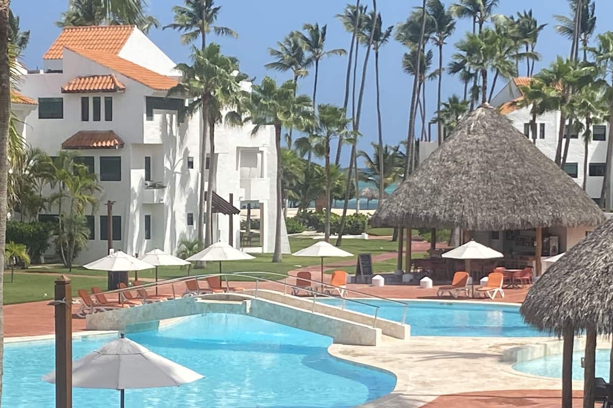 A resort with a large pool area, lounge chairs, and thatched umbrellas.