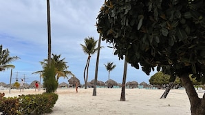 Una playa con palmeras, cabañas de techo de paja y cielo despejado.