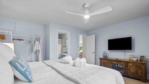 Une chambre à coucher avec un grand lit, un ventilateur de plafond, une télévision et une commode en bois.