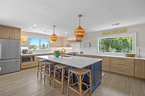 Une cuisine moderne dotée d’un grand îlot central, de meubles en bois et offrant une vue sur la plage.