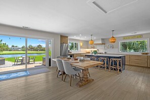 Une cuisine moderne dotée d’un grand îlot central, un coin repas offrant une vue sur un lac, et une pancarte indiquant « MAISON DE VACANCES AU BORD DE LA PLAGE ».