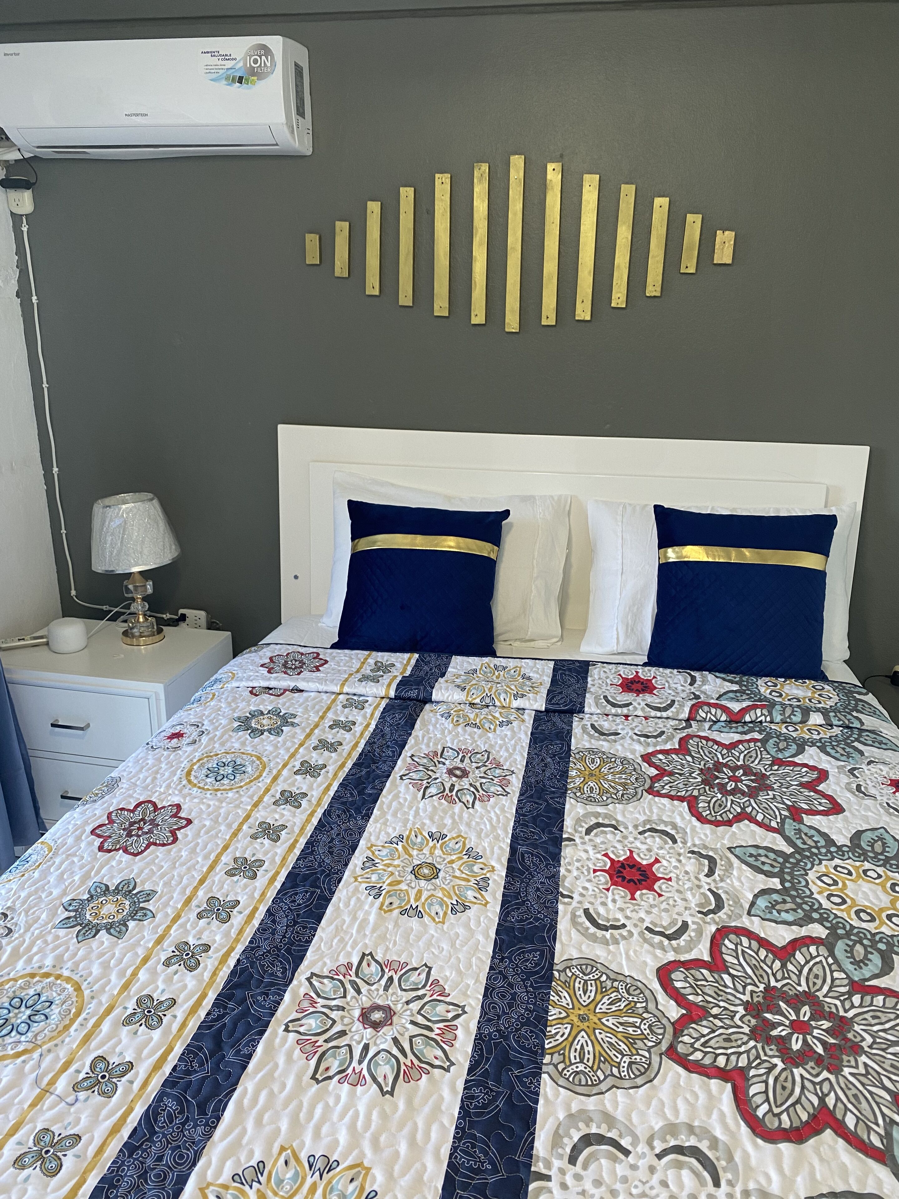 Una cama bien hecha con colcha de estampado floral, cabecera blanca y dos almohadas con adornos dorados.