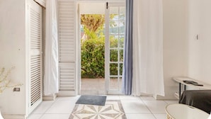 A room with a door leading to a garden, a small table, and a bed.