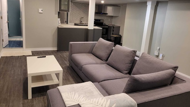 A modern living room with a grey sofa, a white coffee table, and a kitchen in the background.