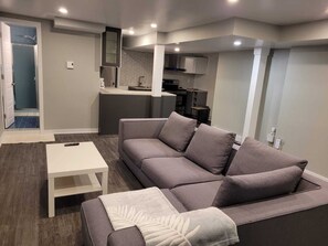 A modern living room with a grey sofa, a white coffee table, and a kitchen in the background.