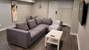 A modern living room with a grey sectional sofa, a white coffee table, and a flat-screen TV mounted on the wall.