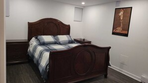 A bedroom with a wooden bed, a bedside table, a wall-mounted picture, and a window with blinds.