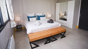 Une chambre d’hôtel moderne avec un grand lit, un banc, une armoire et un miroir.
