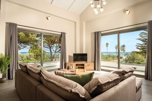 Un salon moderne avec un canapé, une table basse, un téléviseur et de grandes fenêtres offrant une vue sur la mer.