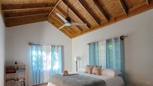 A spacious bedroom with a wooden ceiling, a large bed with a grey and white duvet, a bedside table, and a wooden nightstand.
