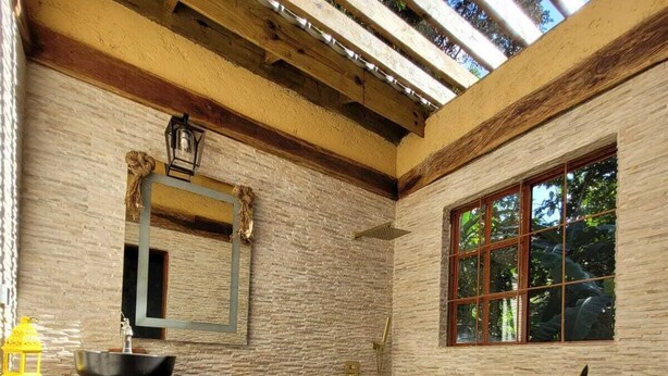 A rustic bathroom with a stone wall, a wooden vanity, a mirror, and a window.