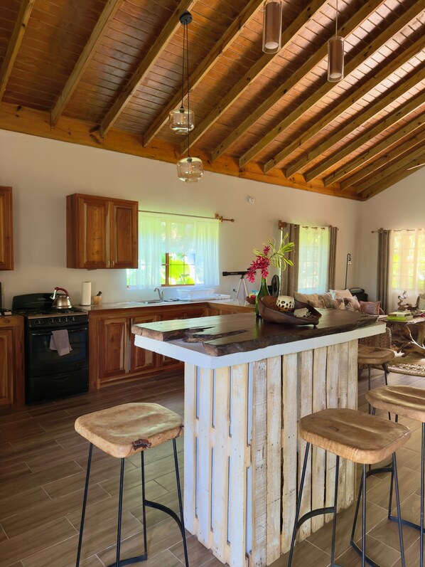 A rustic kitchen with wooden beams, a large island with stools, and a view of the outdoors through large windows.