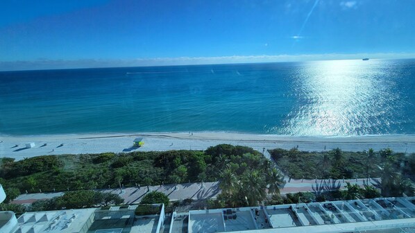 A beach view from a high vantage point, including a parking area with a few cars and a lifeguard station.