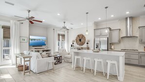 A spacious living area with a large island, white furniture, and a ceiling fan. - 3BR Prominence 30A Townhome Near Pool, Sleeps 10 - Spring openings (Watersound)