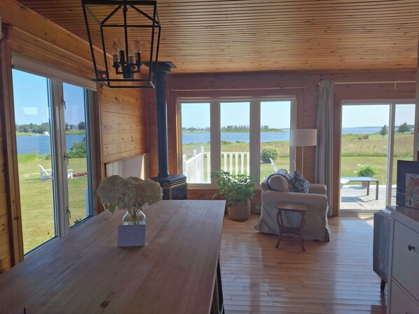Een houten interieur met een groot raam met uitzicht op een meer, een eettafel met een bloevas en een bank met panoramisch uitzicht.