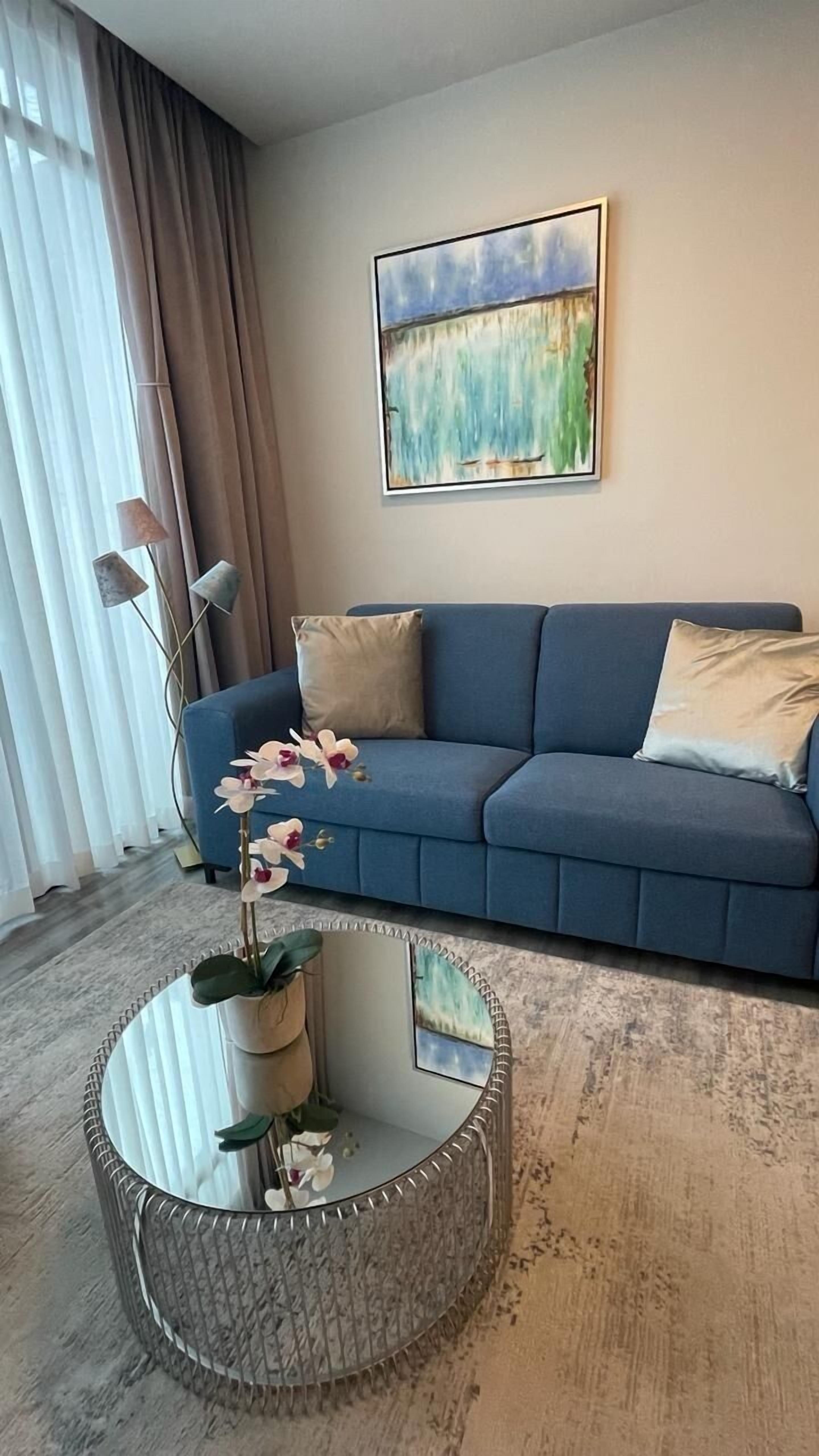 A living room with a blue sofa, a round coffee table with a plant, and a painting on the wall.