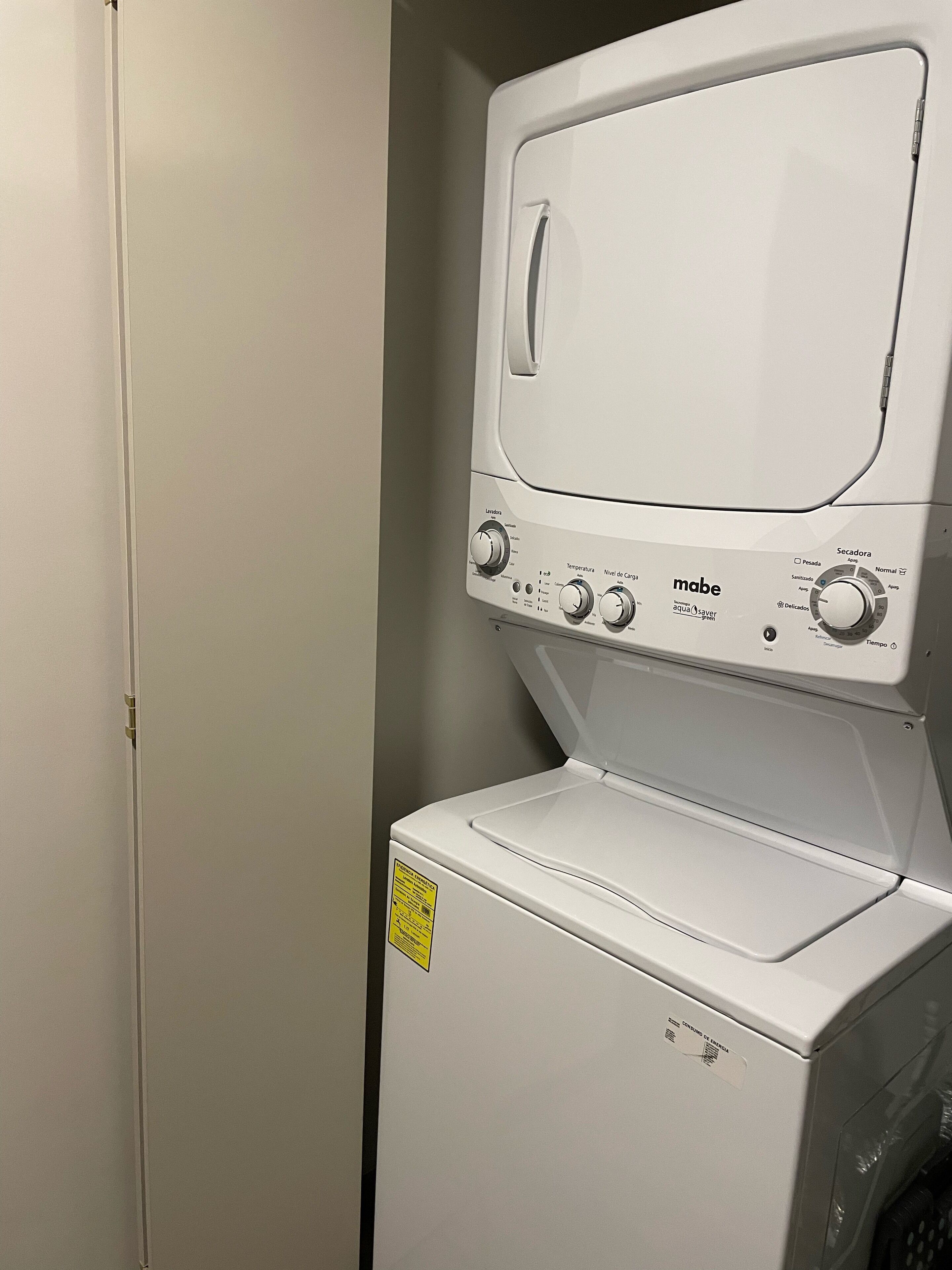 A front-loading white washing machine with control knobs and a yellow sticker on the door.