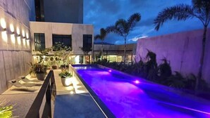 A modern outdoor pool area with a long, narrow pool illuminated by purple lights, surrounded by potted plants and a concrete wall. - Cozy apartment with terrace Cosmopolitan Tower, Nunciatura, San Jose (San José)