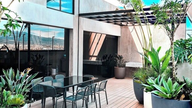 An outdoor patio with a glass table and chairs, surrounded by potted plants and a view of the cityscape. - Cozy apartment with terrace Cosmopolitan Tower, Nunciatura, San Jose (San José)