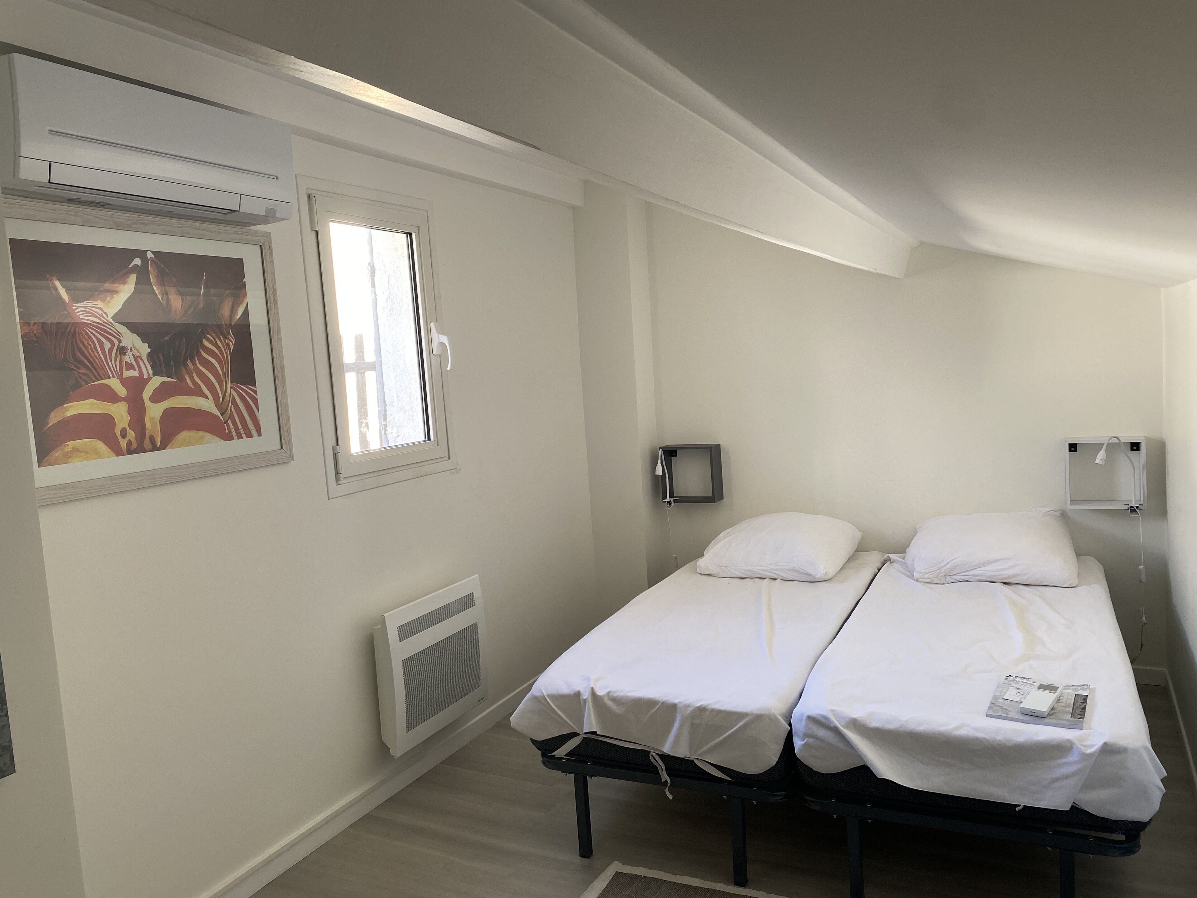 Een kleine, schone kamer met twee eenpersoonsbedden, een raam, een radiator en een wandlamp.