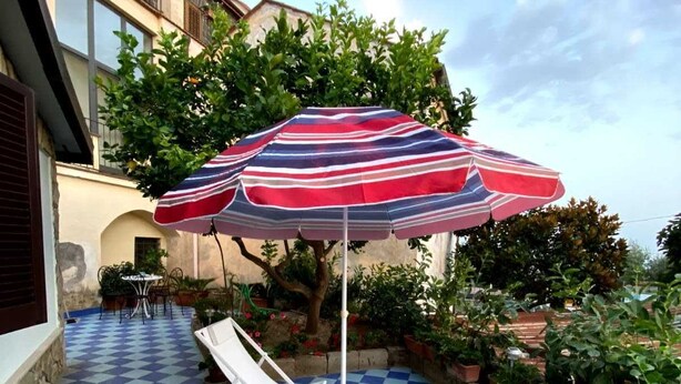 Una veranda esterna a scacchi con due poltrone blu e un ombrellone a righe.