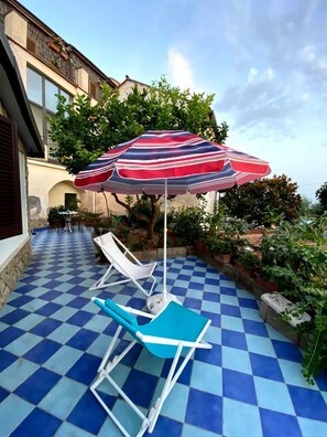 A checkered outdoor patio with two blue lounge chairs and a striped umbrella.