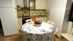Una cucina compatta con pensili e basi bianchi, un piano cottura a gas e un lavello. Un tavolo da pranzo con tovaglia bianca e sedie è posto al centro.