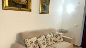 Un soggiorno con un divano color beige, cuscini decorati e due quadri appesi al muro.