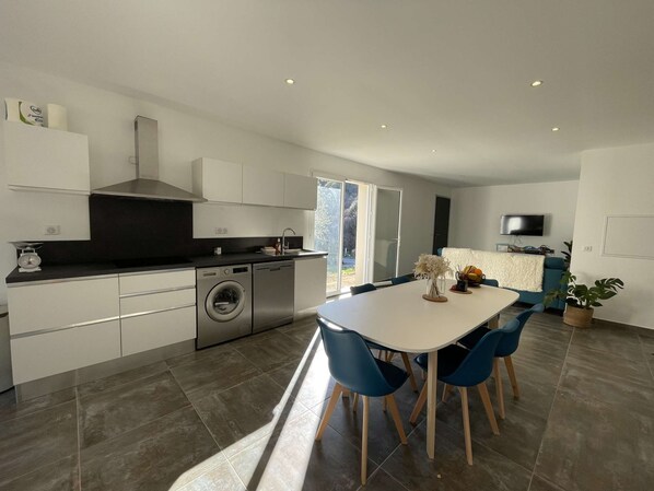 Una cocina moderna con lavadora y secadora integradas, un comedor con sillas azules y un televisor montado en la pared.