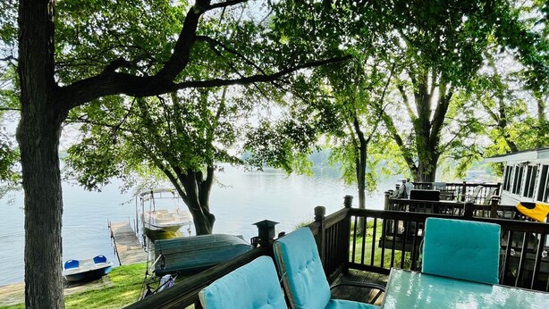 Un espacio de estar al aire libre con vistas a un lago, una lancha amarrada cerca y una mesa con una taza verde.