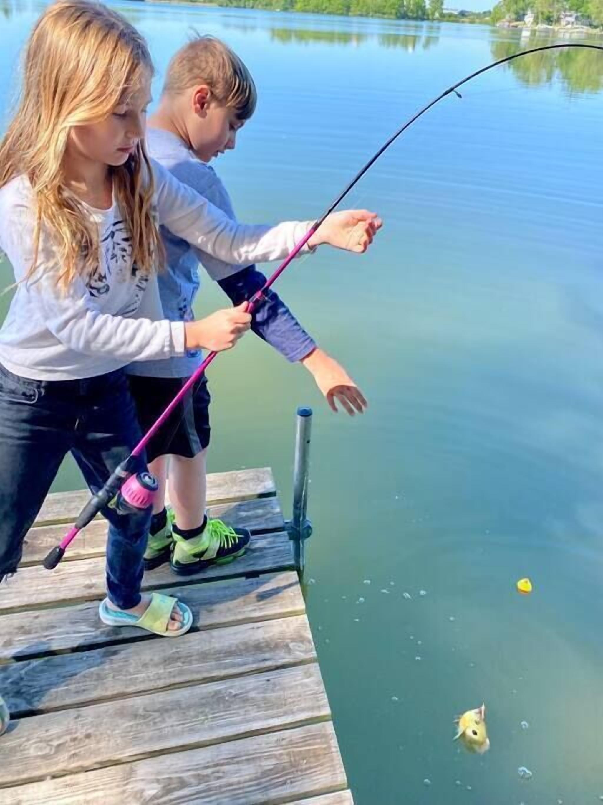 Two individuals fishing on a wooden dock extending into a calm lake.