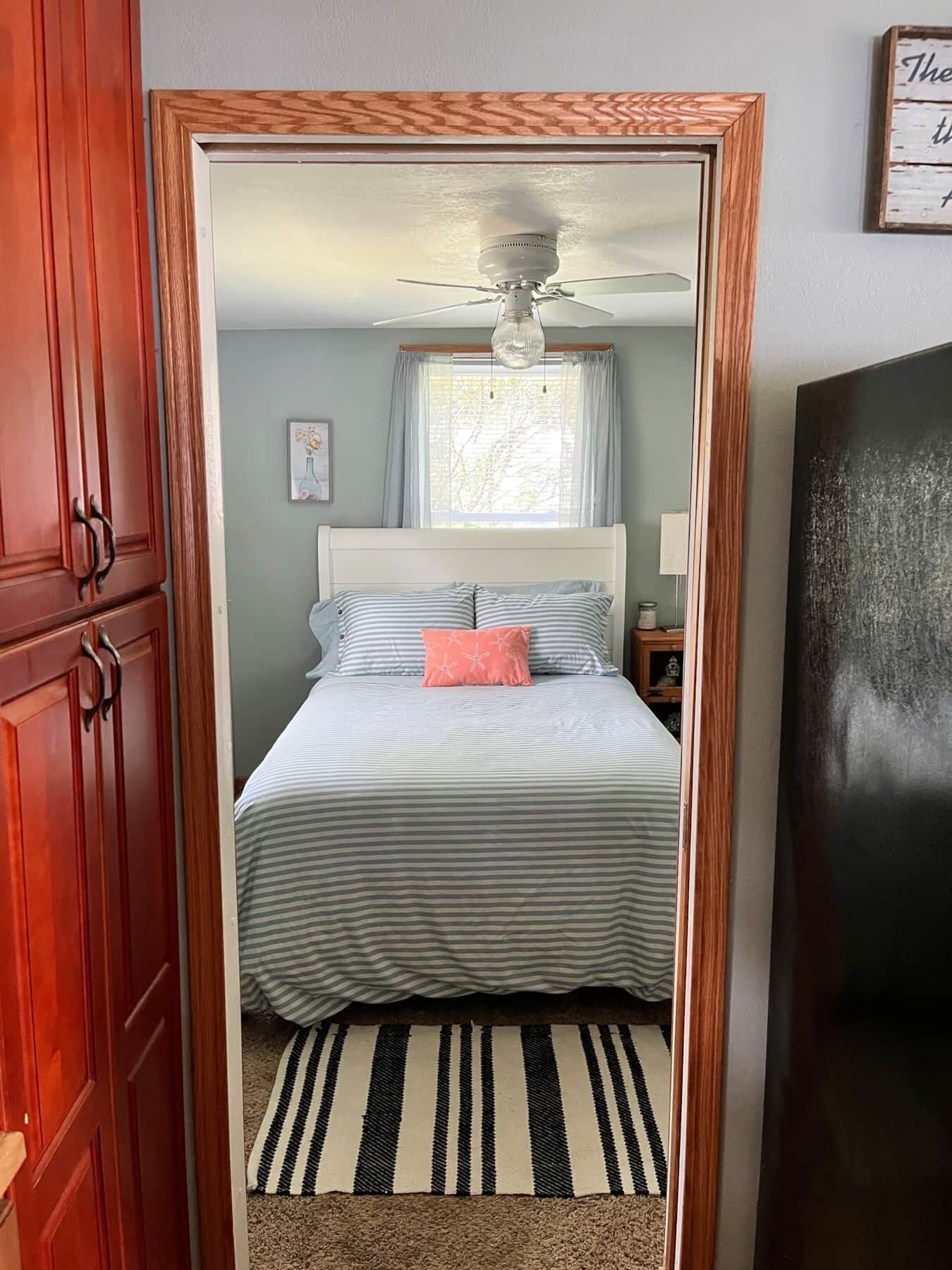 Un dormitorio con una cama, una mesita de noche, una lámpara, un ventilador de techo y una ventana con cortinas.