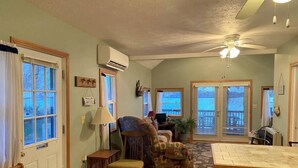 Un salón amplio con un gran ventanal, ventilador de techo y comedor con mesa y sillas de madera.
