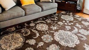 Una sala de estar con un sofá gris, un televisor de pantalla plana, un pez decorativo y un tapete floral.