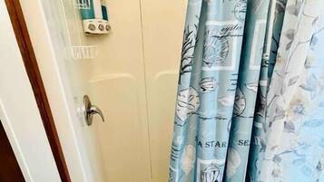 Un espace douche doté d’une porte en verre, d’un pommeau de douche à main et d’un ensemble de produits de toilette fixés au mur.