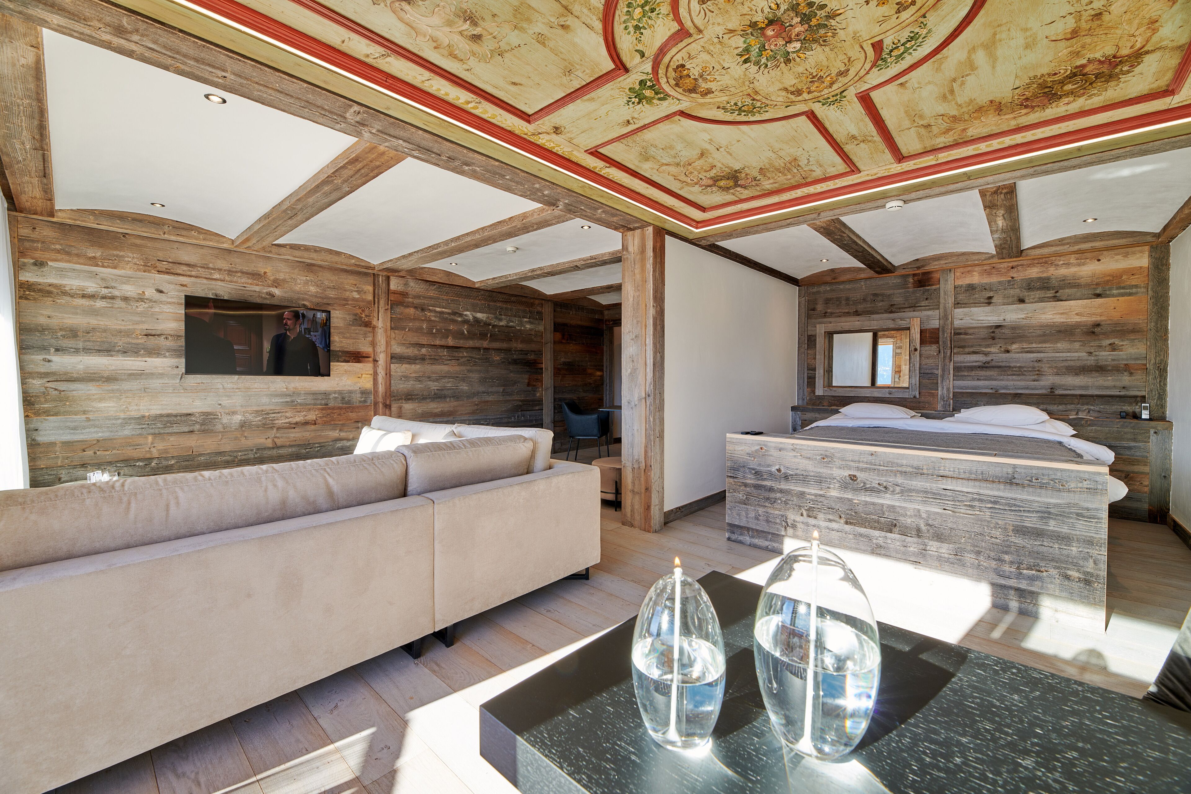 A modern interior with a wooden ceiling, a sofa, a bed, and a glass table.