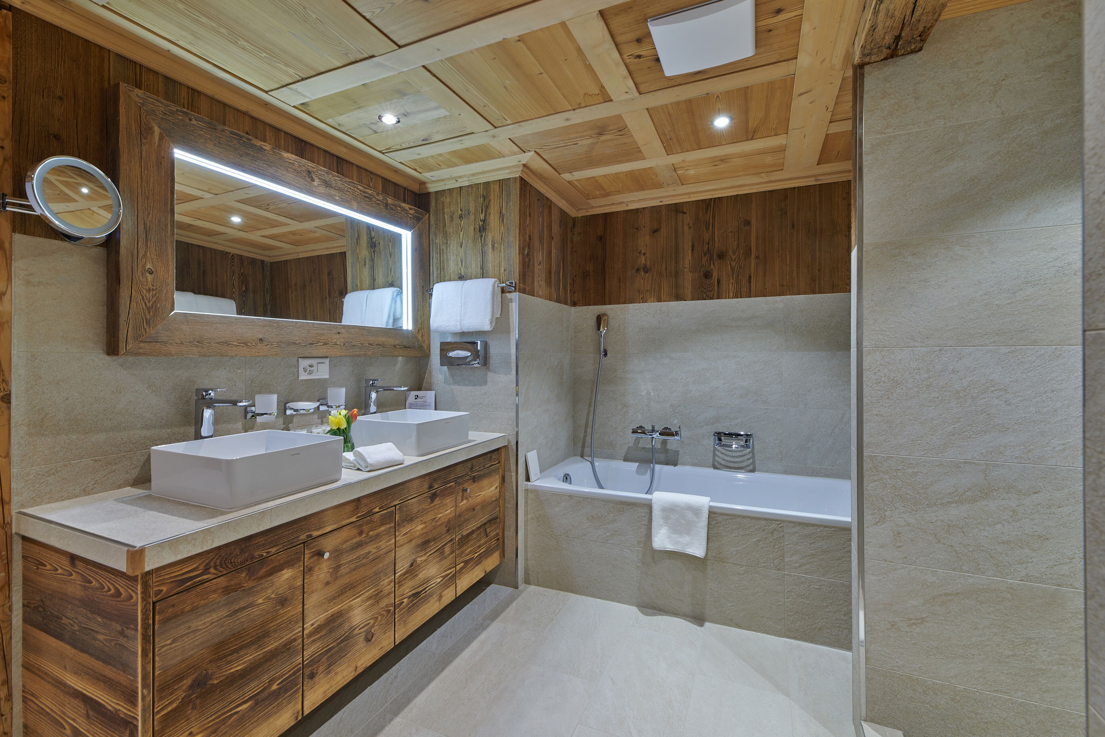 Un baño moderno con muebles de madera, un espejo grande, dos lavamanos, una bañera y una ducha.