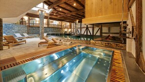 A spa area with a hot tub, lounge chairs, and a stone wall. - Aïda Hôtel & Spa (Adults Only) (Crans-Montana)