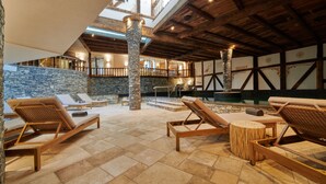 A sunlit lounge area with stone pillars, wooden beams, and a stone wall. - Aïda Hôtel & Spa (Adults Only) (Crans-Montana)