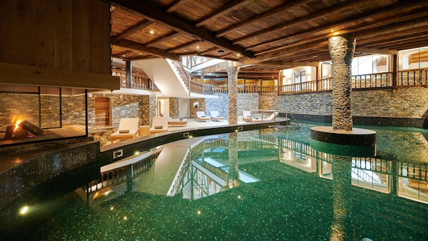 A spacious indoor pool with a stone pillar, wooden beams, and a stone wall. - Aïda Hôtel & Spa (Adults Only) (Crans-Montana)
