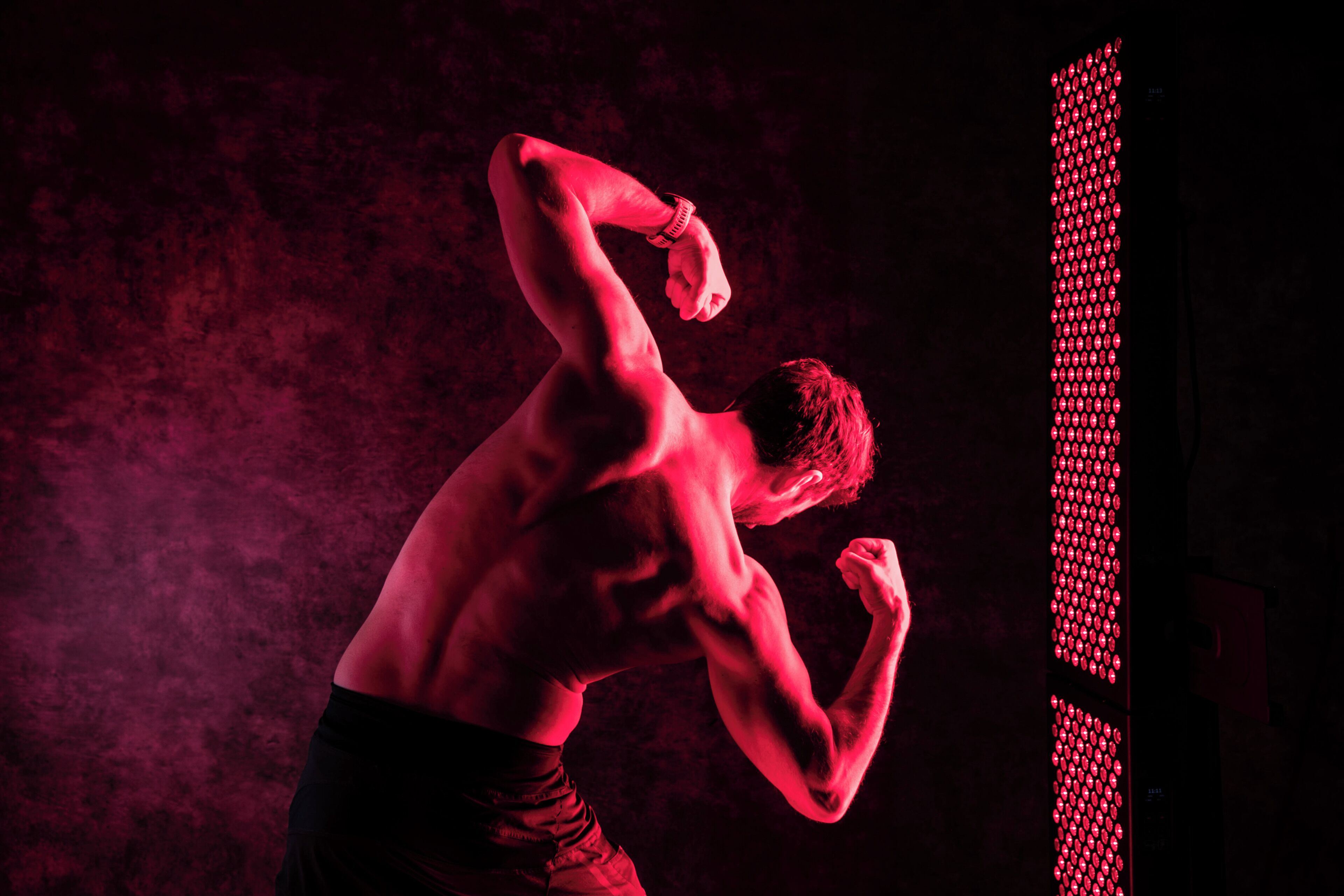 A person in a dynamic pose, possibly in a gym or training area, with a dark background and red lighting.