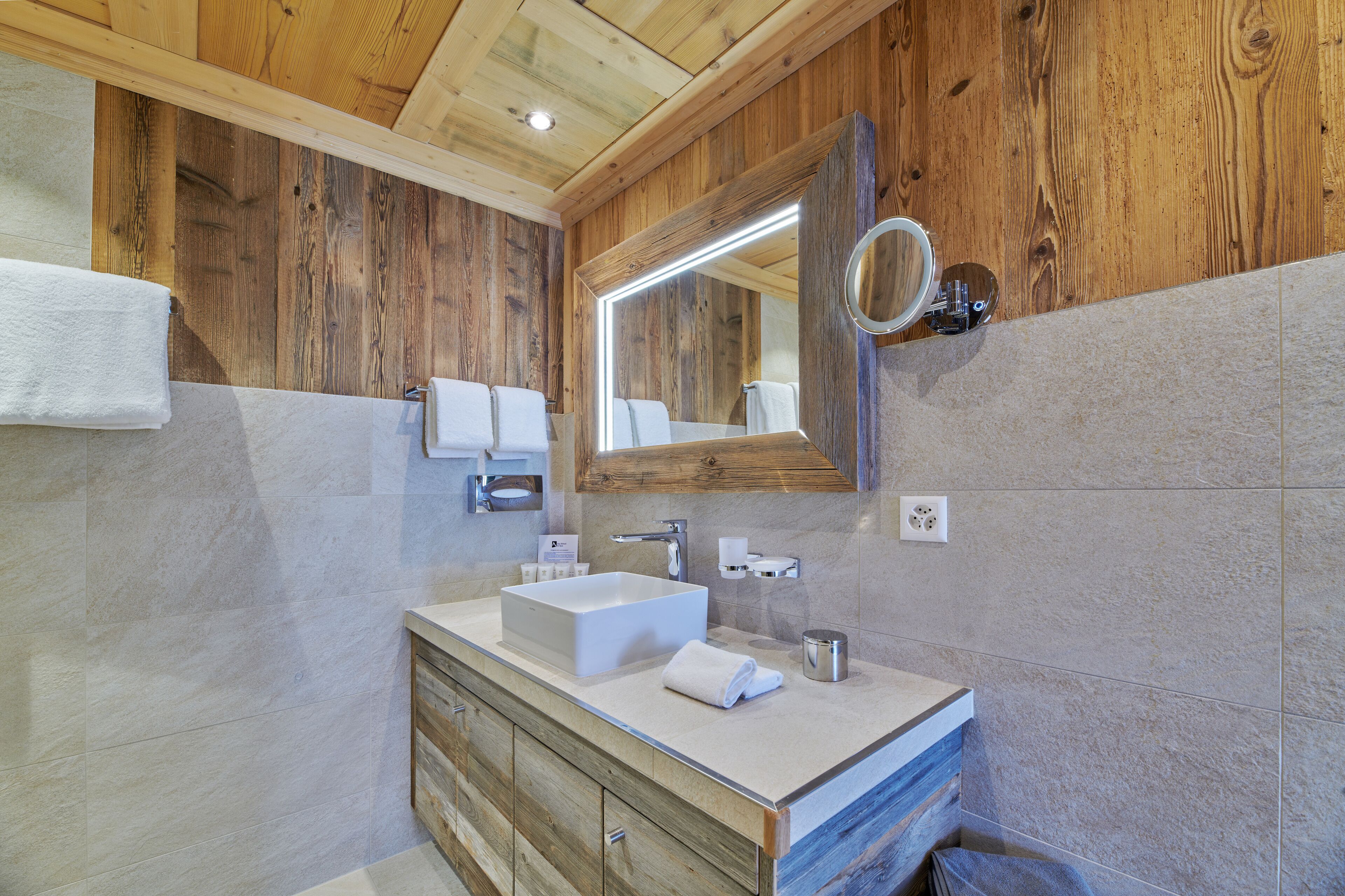 A bathroom with a wooden ceiling, a large mirror, a white sink, and a wooden cabinet.