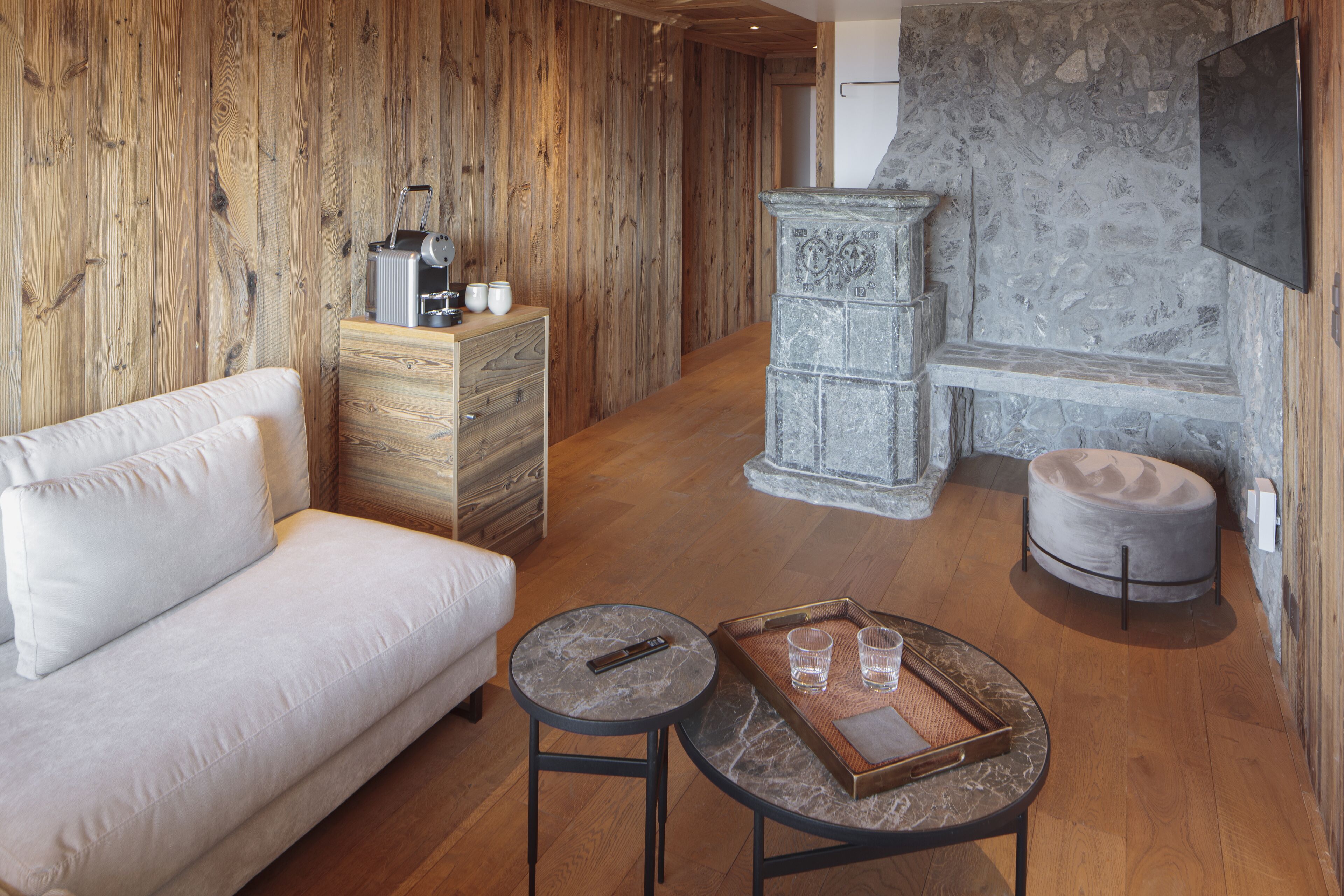 Ein gemütliches Zimmer mit Holzboden, einem weißen Sofa, einem kleinen runden Tisch mit Tablett und einem Kamin aus Stein.