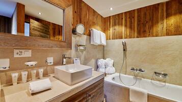 Une salle de bain moderne avec un mur recouvert de panneaux en bois, un grand miroir, un lavabo blanc, une baignoire et un meuble-lavabo avec des articles de toilette.