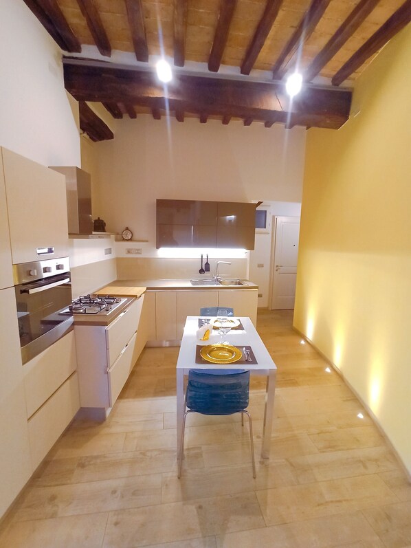 Une cuisine compacte dotée d’appareils électroménagers modernes, une table à manger pour deux personnes et un plafond en bois.