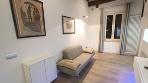 Ein Wohnzimmer mit einer Couch, einer Heizung, einem gerahmten Bild und einem Fenster mit Vorhängen.